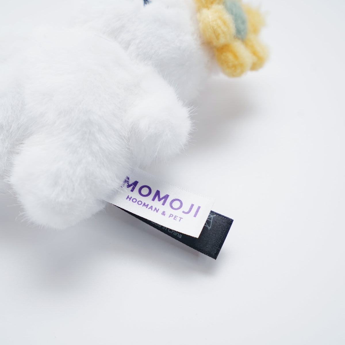 Close-up of the cream Momoji Bear plush and its label